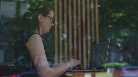 Female freelancer sits in cafe working in laptop view from street through window Stock Footage 280364899