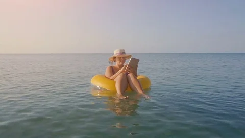 Female freelancer with a tablet on inflatable ring in the sea Stock Footage 80551272