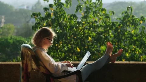 Female freelancer using laptop sitting on the roof terrace in sunlight. Stock Footage 236682931