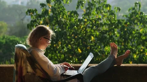 Female freelancer using laptop sitting on the roof terrace in sunlight. Stock Footage 237622314