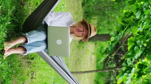 Female freelancer wearing hat using a laptop outdoors. Видео 244634972