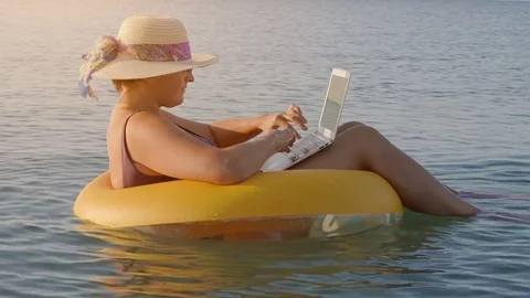 Female freelancer works on a laptop sitting in an inflatable ring in the sea, Stock Footage