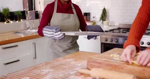 Female friends baking, oven timer dinging, woman in maroon with mitts presenting Stockbeeldmateriaal 345607187