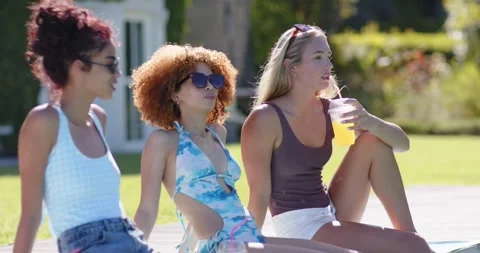 Female friends chatting on pool deck, sipping cup, noticing off-camera movement, Stock Footage 339163172
