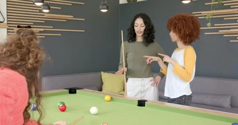 Female friends discussing angles at pool table, urging third striking cue Stock Footage 344104800