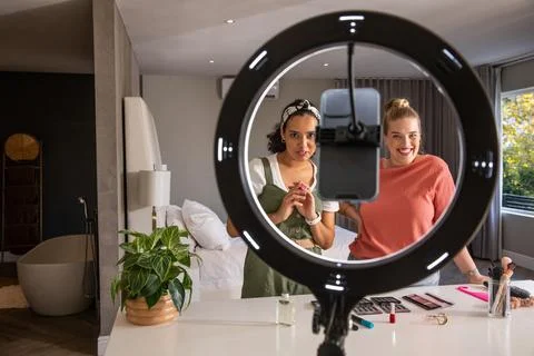 Female friends filming makeup tutorial with smartphone mount under ring light in 스톡 사진