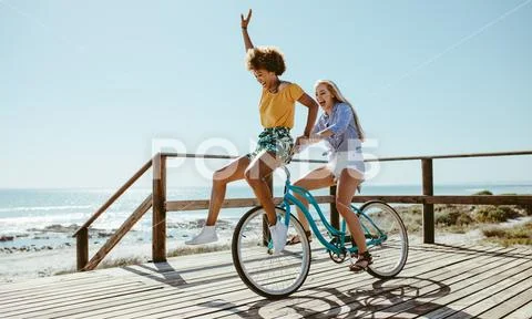Female friends having fun on a bike at beach Stock Photos
