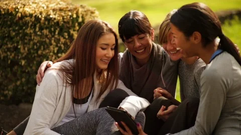 Female friends looking at a tablet while sitting outside Vidéo 88406253