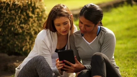 Female friends looking at a tablet while sitting outside Vidéo 88444658