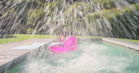 Female friends playing, jumping into pool, splashing woman on pink float holding Stock Footage 338326360