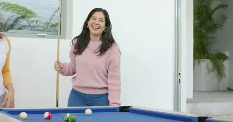 Female friends playing on pool table in game room laughing upon friend entering Stock Footage 344330835