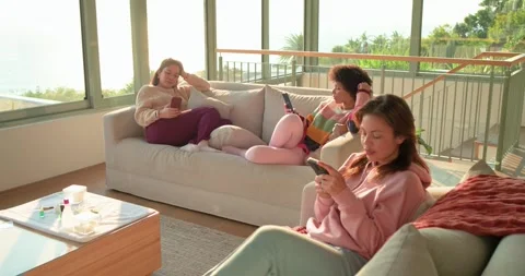 Female friends pulling red blanket on sofas for warmth in lounge by ocean Stock Footage 335198888