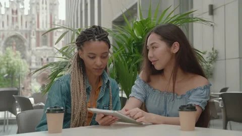 Female friends sitting outside while chatting and looking at tablet. Students in Stock Footage 165004147