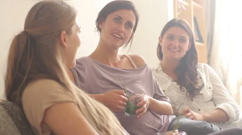 Female friends sitting on sofa drinking tea and chatting Stock Footage