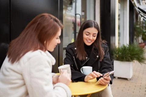 Female friends smiling while using a mobile phone sitting at coffee shop Foto stock