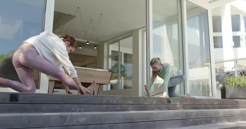 Female friends stepping on deck unrolling mats lunging stretching hamstrings by Stock Footage 340454368
