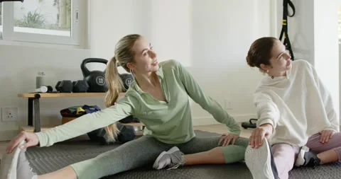 Female friends warming up, holding side bends and circling hips on rubber mat at Stock Footage 342392374