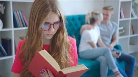Female geek is reading tutorial while couple hugging on the couch at the library Stock Footage 106440162