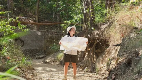 Female geologist using a map, examining a natural path in forest Stock Footage 226475677