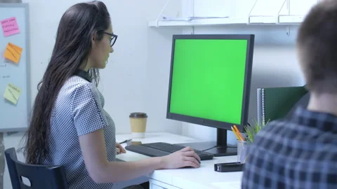 Female with glasses in front of large computer monitor with green screen Stock Footage 142215676