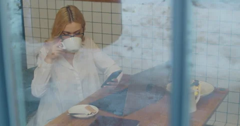 Female in glasses using app on smartphone and drink tea in a cafe. View through Stock Footage 149986052