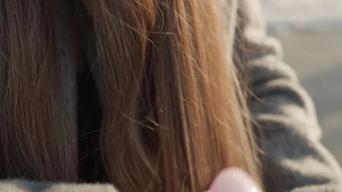 Female in gray coat combing her flowing hair during winter. Park visitor with Stock Footage 342430872