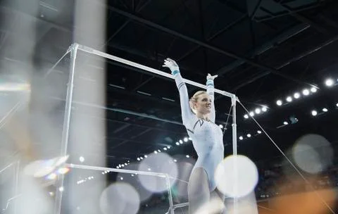Female gymnast with arms raised below uneven bars in arena Stock Photos