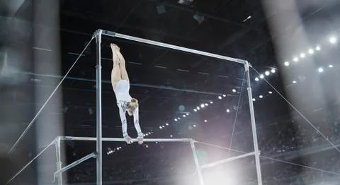 Female gymnast performing on uneven bars in arena Stock Photos