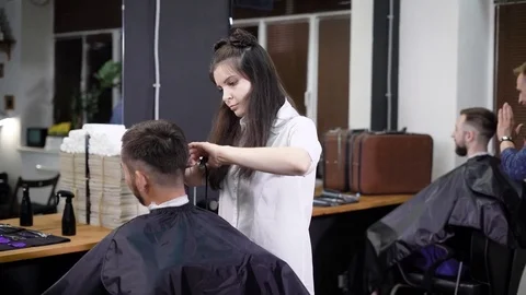 Female hairdresser at work. Male customer sitting on the chair, and other barber Stock Footage