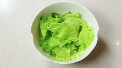 Female hand adding to a cut lettuce pieces of fried bacon and avocado. Salad Stock Footage 107395665