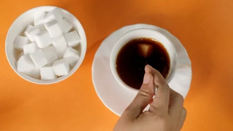 Female hand adding a sugar cube into a hot cup of black coffee before serving Stock Footage 158977335