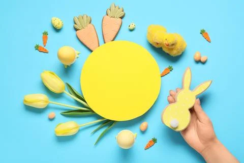 Female hand with blank card, Easter eggs and tulip flowers on blue background Stock Photos