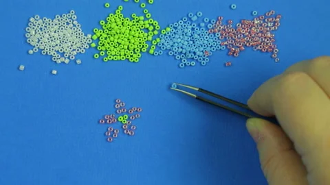 Female hand on a blue background beads patterns of flowers with tweezers. Close 스톡 동영상 99252597