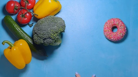 Female hand chooses between donut and vegetables decides to take fresh pepper Video stock 123782802