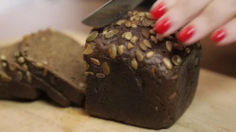 Female hand cuts bread with bran with a knife on a wooden board Stock Footage 130032394