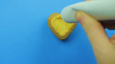 Female hand draws funny emoticons on heart shaped cookies on a blue background Stock Footage 98604341