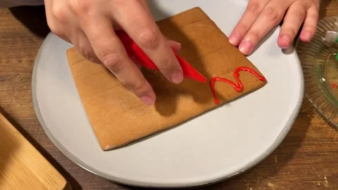 Female hand draws red wave pattern on gingerbread house roof in plate Stock Footage 340427763