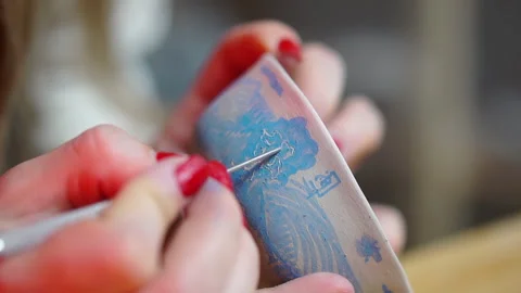 Female hand engraves with a metal stack the blue ceramic clay bowl Stock Footage 256325357