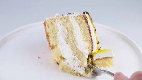 A female hand with a fork breaks a piece of banana cake on a white plate or Stock Footage 194649474