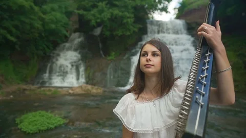 The female hand gently touches the strings of the bandura at waterfall Stock Footage 94961084