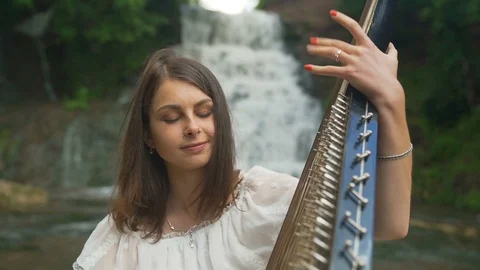 The female hand gently touches the strings of the bandura at waterfall Stock Footage 94963064