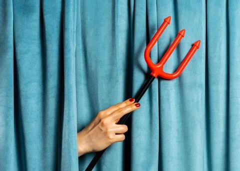 Female hand hold red devil's trident against blue velvet curtains Stock Photos