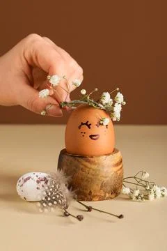 Female hand with holder of creative Easter eggs and flowers on beige table ne Stock Photos