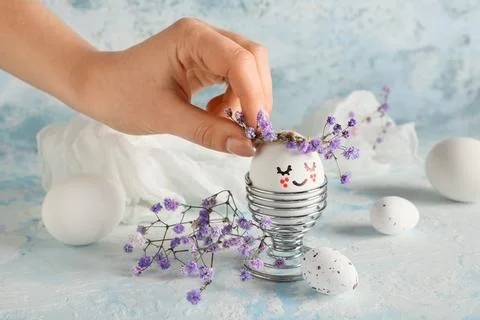 Female hand with holder of creative Easter eggs and flowers on grunge blue ba Stock Photos