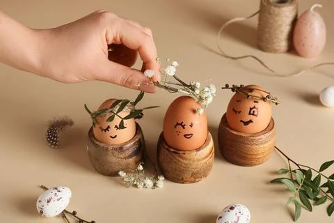 Female hand with holders of creative Easter eggs, leaves and flowers on beige Stock Photos