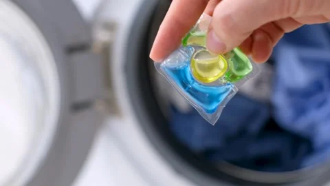 Female hand holding capsule with liquid powder against background of washing Stock Footage 313883445