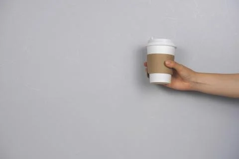 Female hand holding coffee to go blank cup against concrete gray wall copy sp Stock Photos