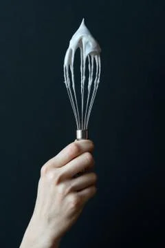 Female hand holding kitchen whisk on a dark background Stock Photos