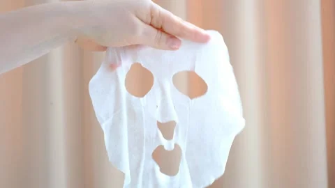 Female hand holding a sheet of moisturizing mask on beige background. Stock Footage 304846320