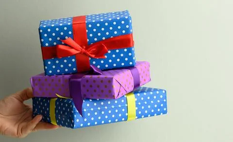 Female hand holding a stack of gift boxes tied with silk ribbon on a gray bac Stock Photos